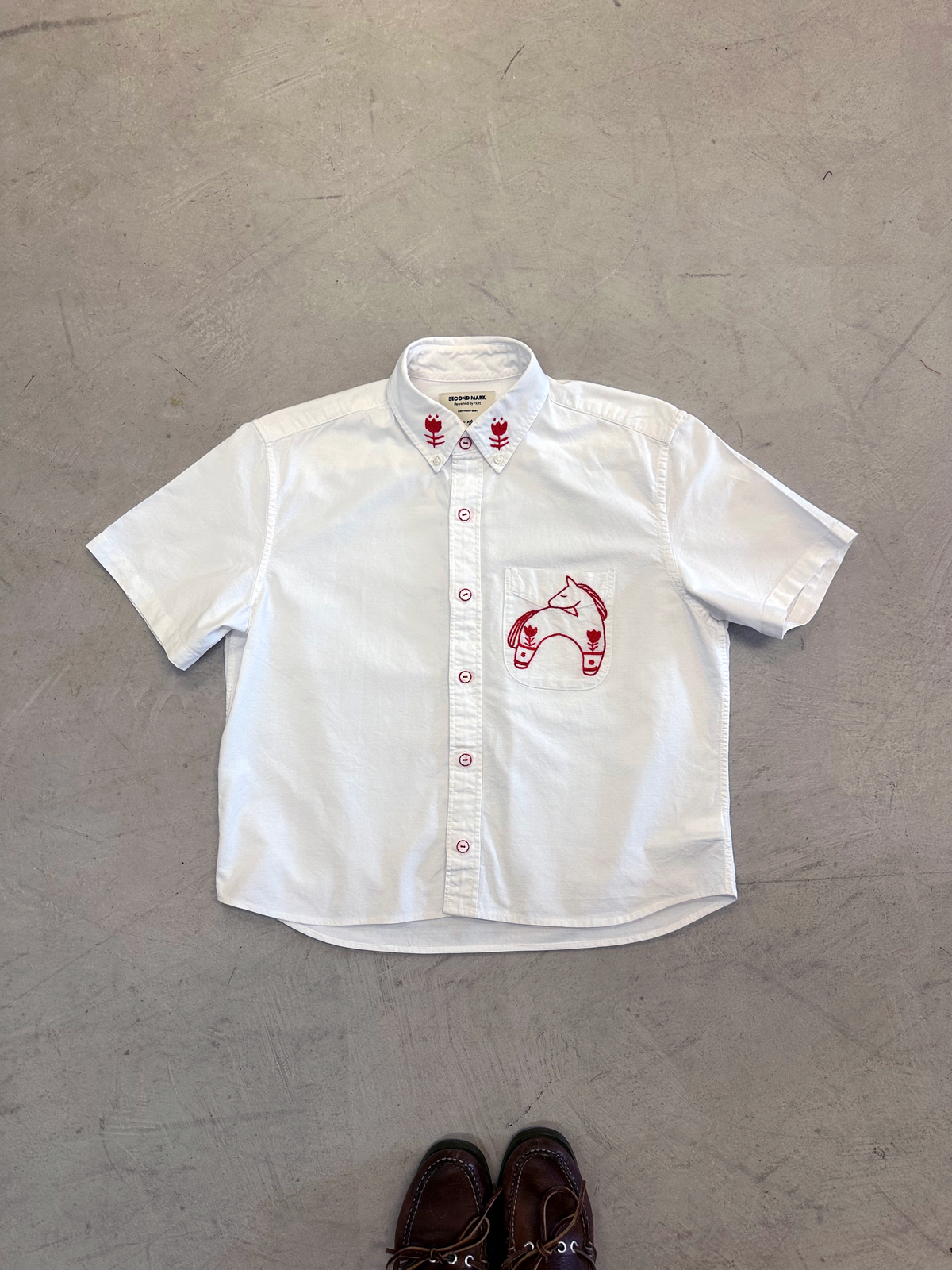White cropped short sleeve button down with a red Dala horse on the chest pocket