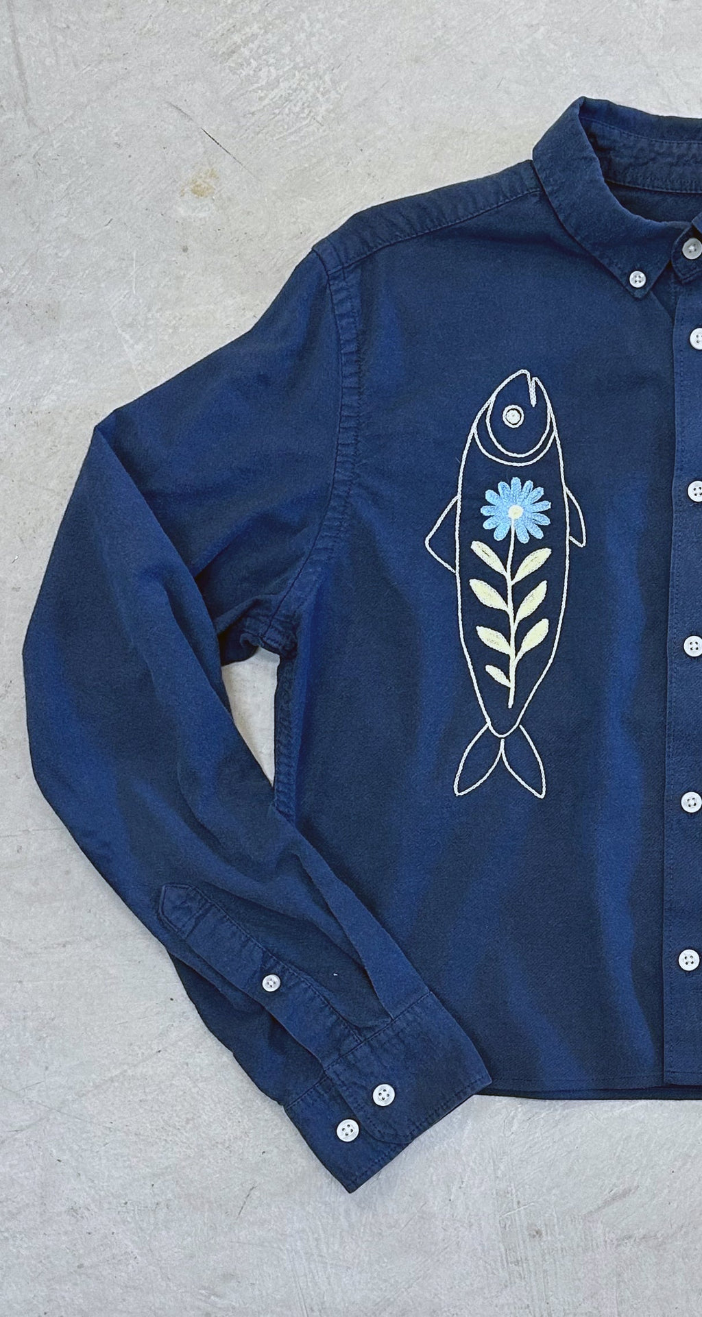 Front view of navy blue cropped button-down with off white fish and blue flower embroidery