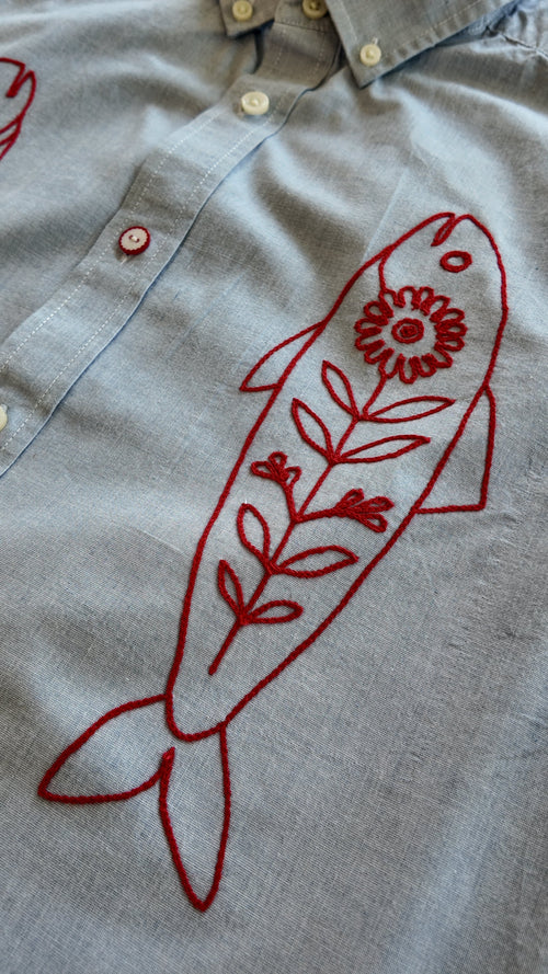 Close-up of red fish chainstitch embroidery detail on grey/blue button-down