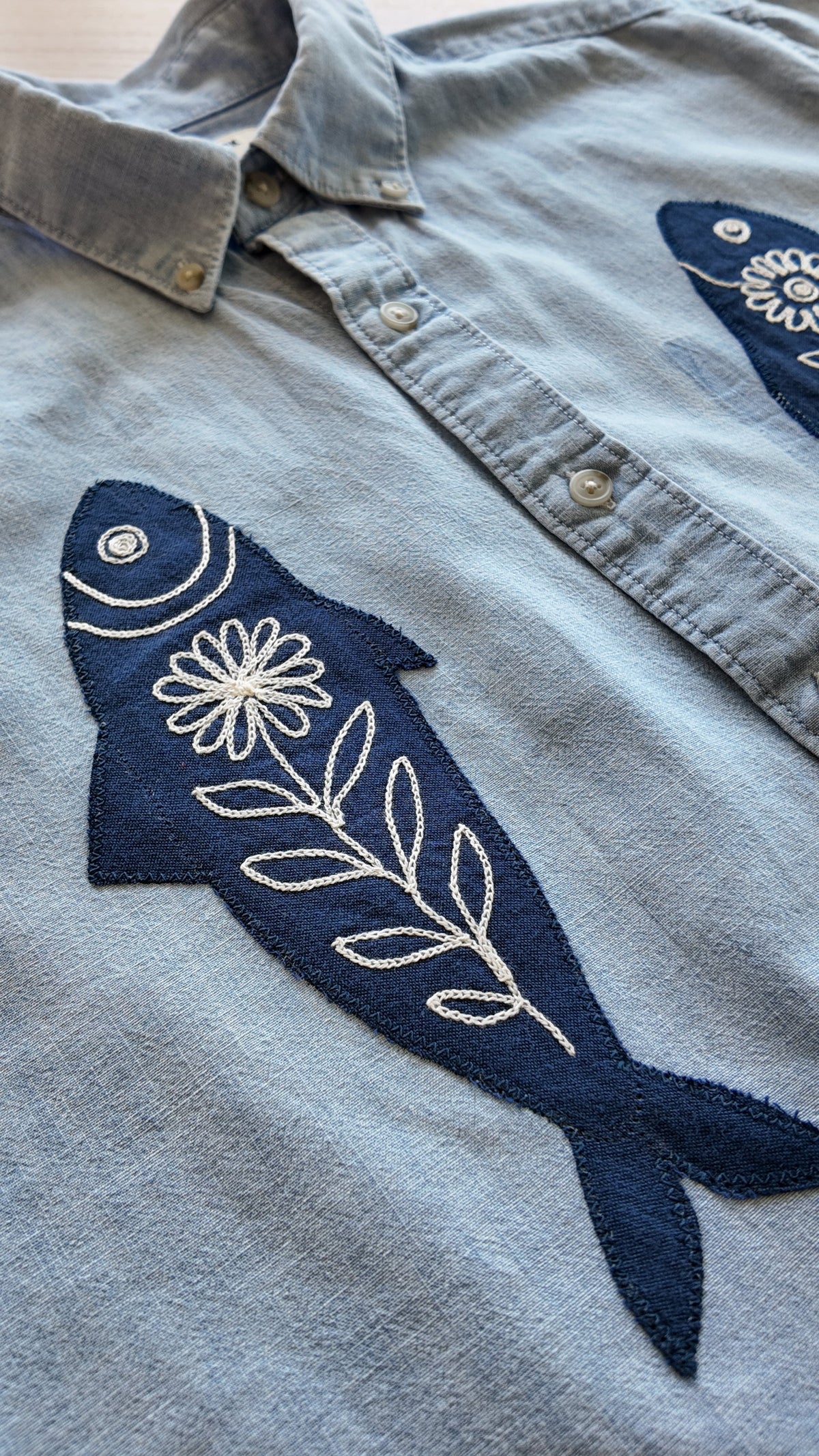 Close-up of navy fish chainstitch embroidery detail on light blue button-down