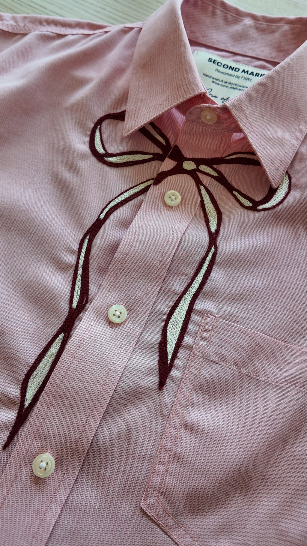 Close-up of maroon and ivory chainstitch bow embroidery detail on pink button-down