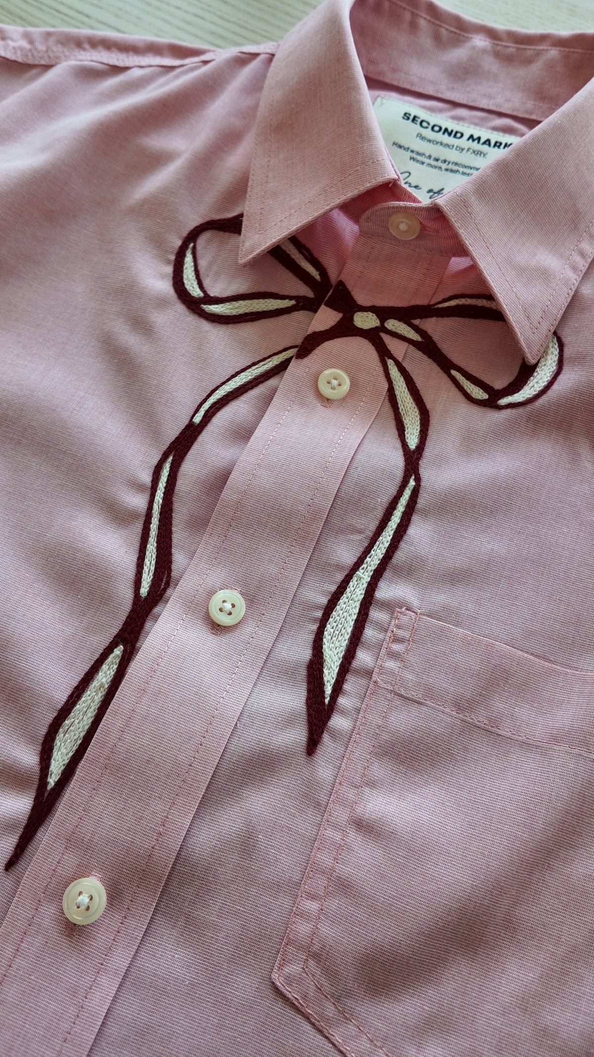 Close-up of maroon and ivory chainstitch bow embroidery detail on pink button-down