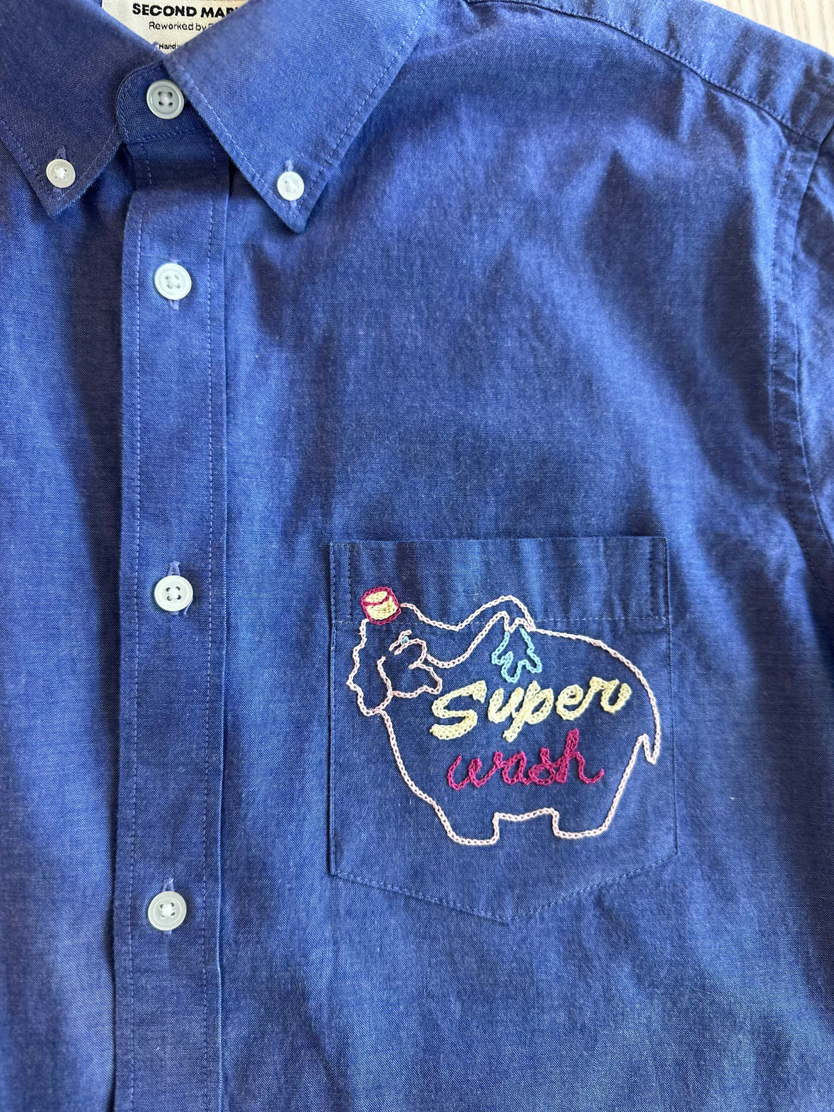 Close-up of pink elephant car wash chainstitch embroidery detail on mid blue button-down